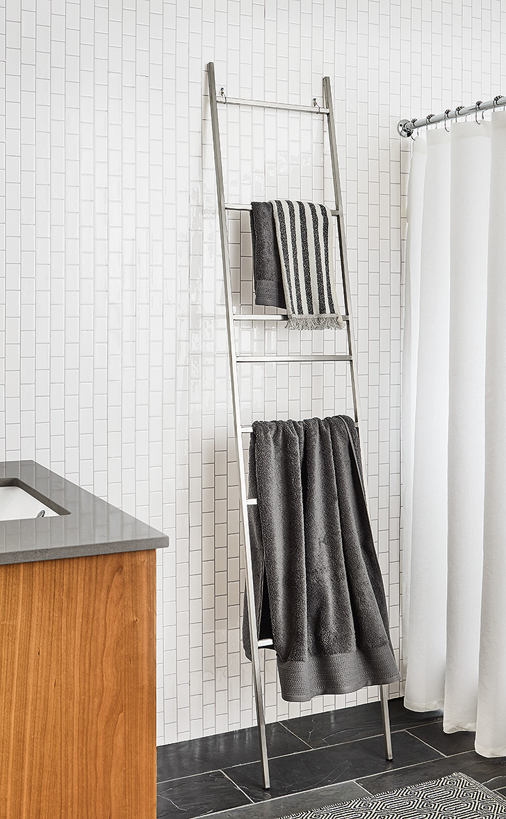 Slim stainless steel ladder holds towels in a modern bathroom