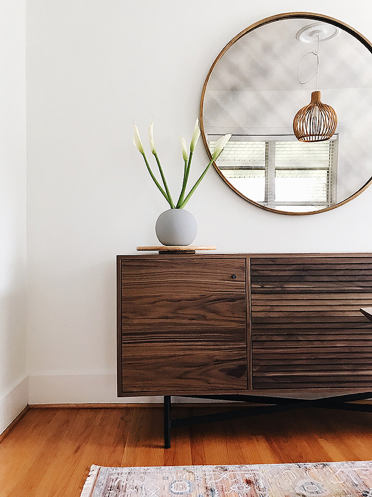 Wood storage cabinet with round mirror above it