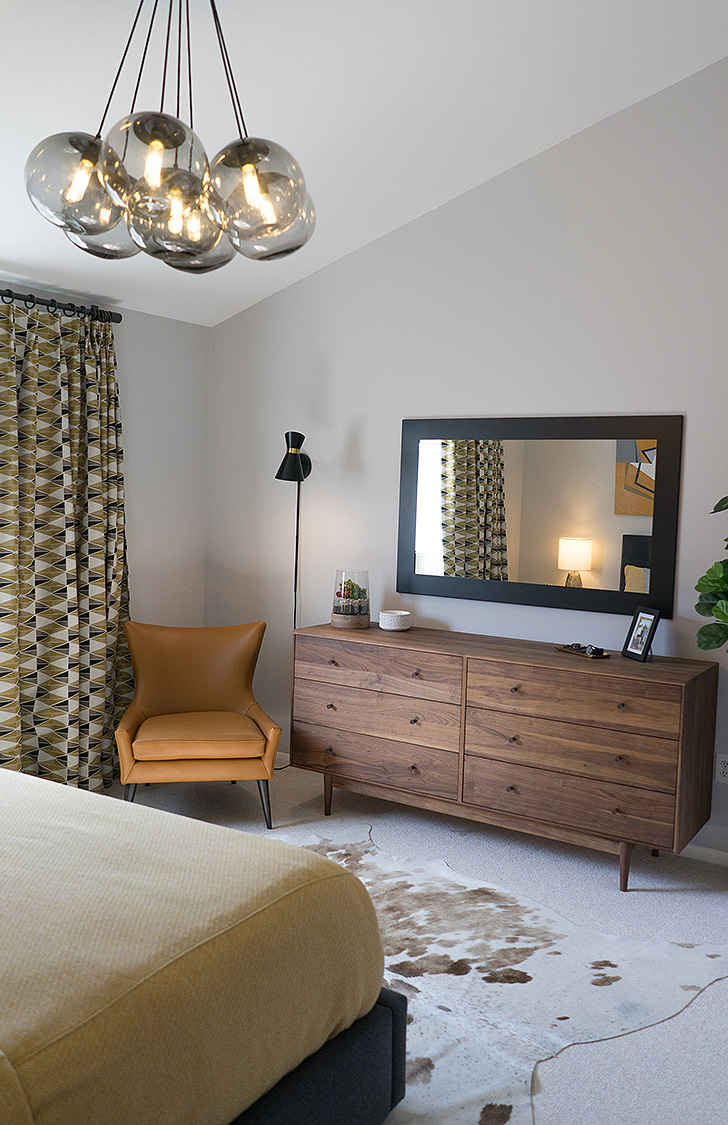 Modern chandelier above leather chair and wood dresser