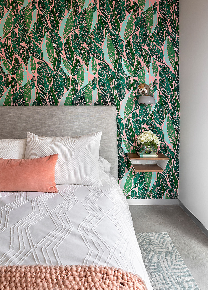 Grey upholstered bed against green and pink wallpaper