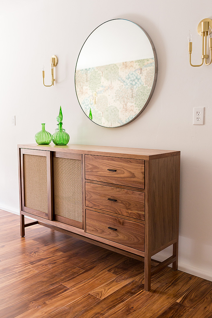 Wood storage cabinet with round wall mirror above it