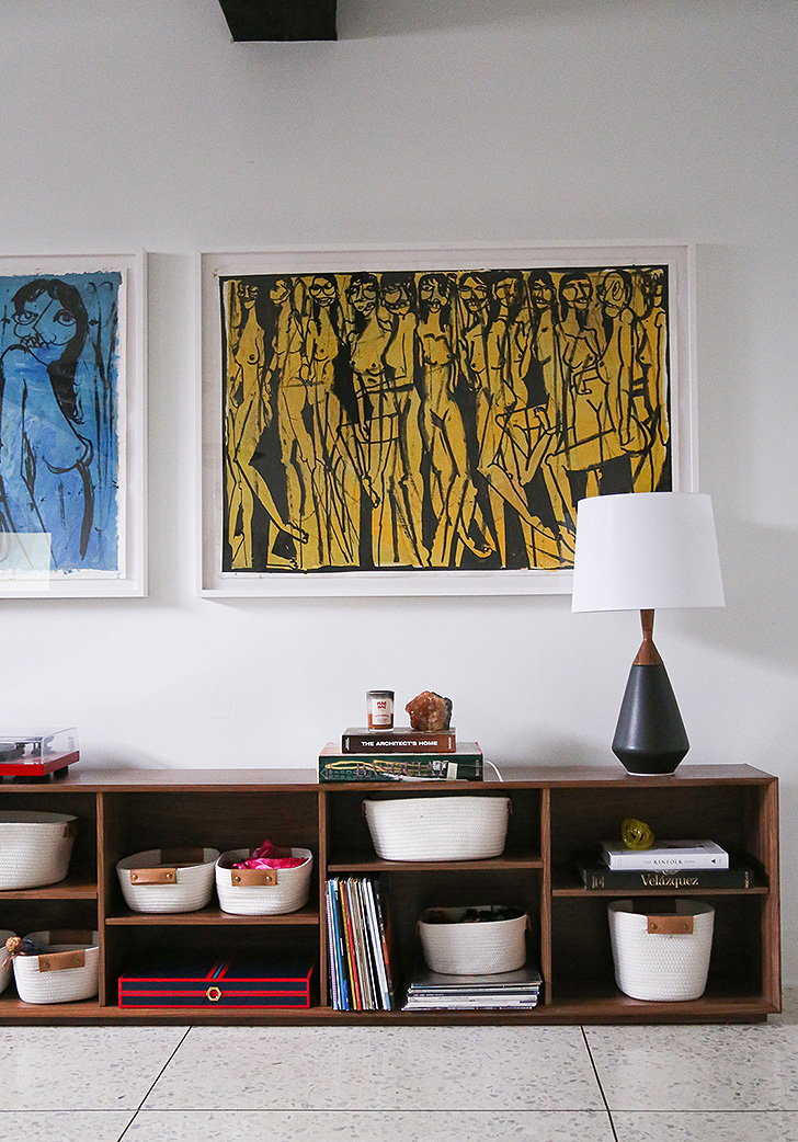 Detail of low, wood bookcases with baskets, books and table lamp