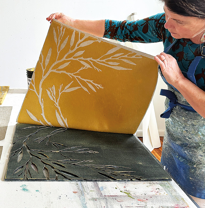 An artist is hand block-printing pillow fabric with a botanical image.