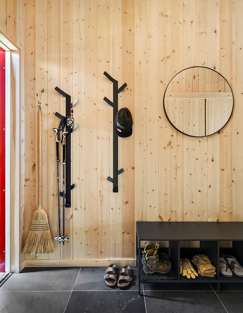 Cabin entryway with modern coat rack, round mirror and cubby bench with shoes.