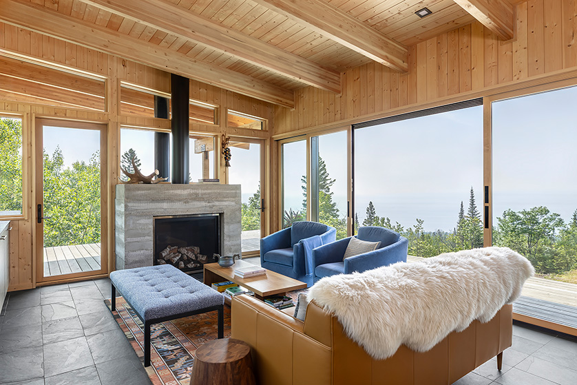 Fireplace area with modern cabin furniture including leather sofa, sheepskin, two chairs, bench and coffee table.